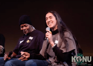 Still from video with Michelle and "Que" holding microphones smiling