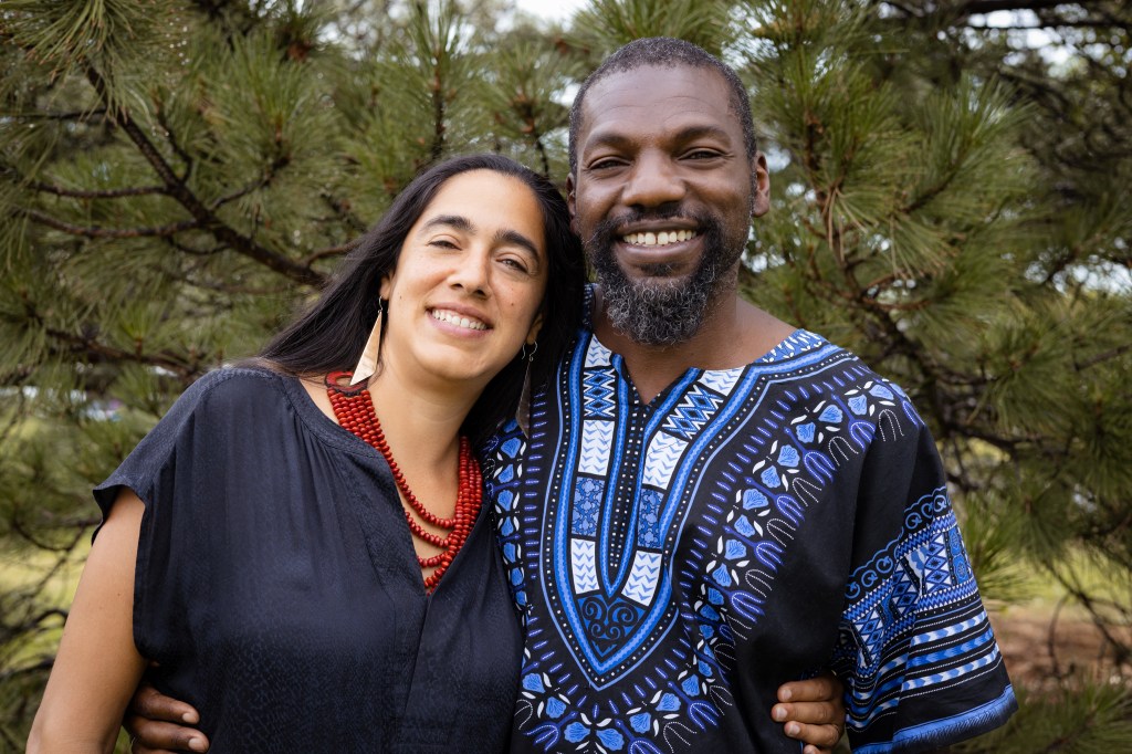 Photo of Ramon and Michelle smiling together in front of large pine